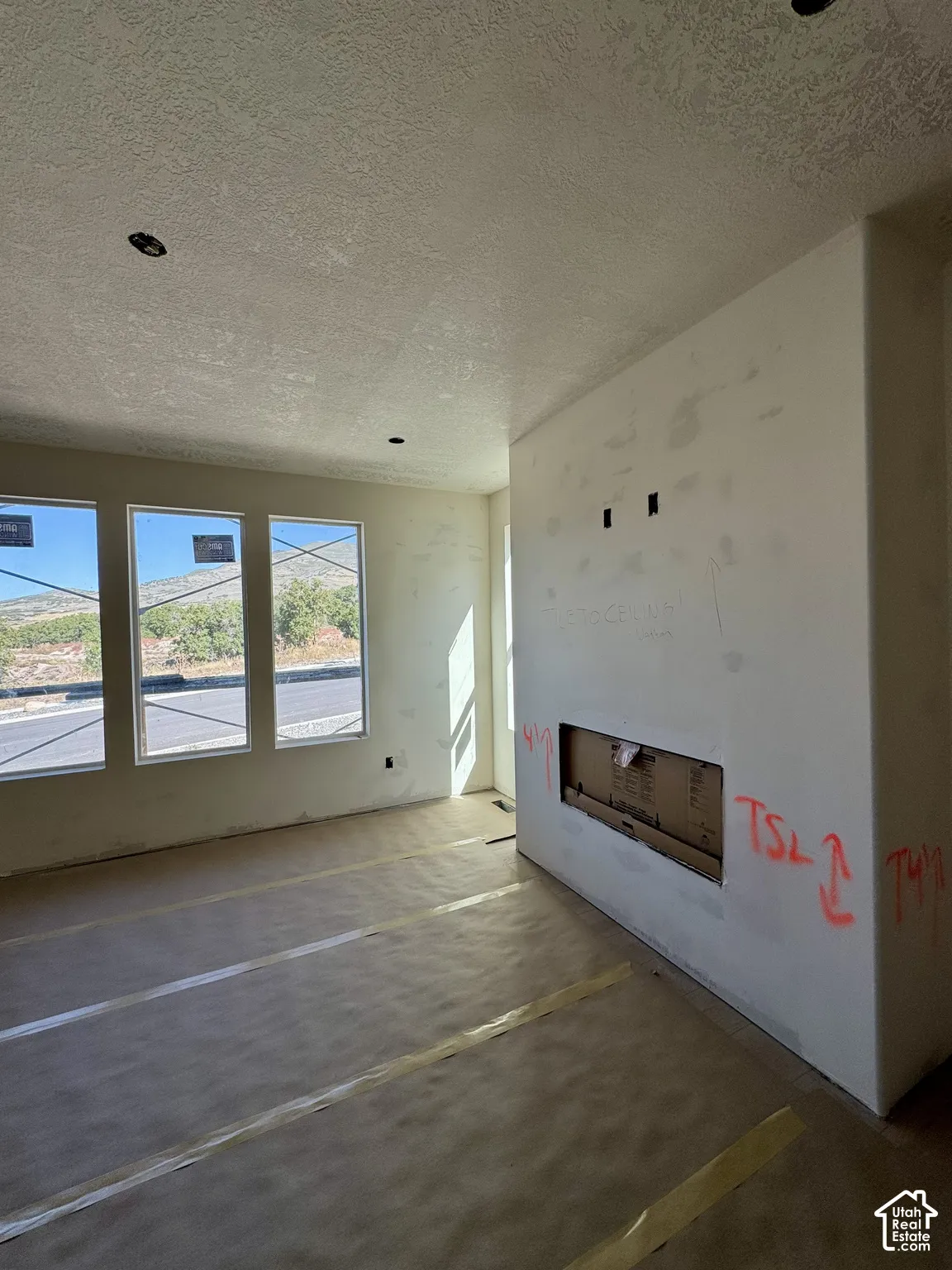 Three large windows, built-in fireplace opening, recessed ceiling lighting, and textured ceilings