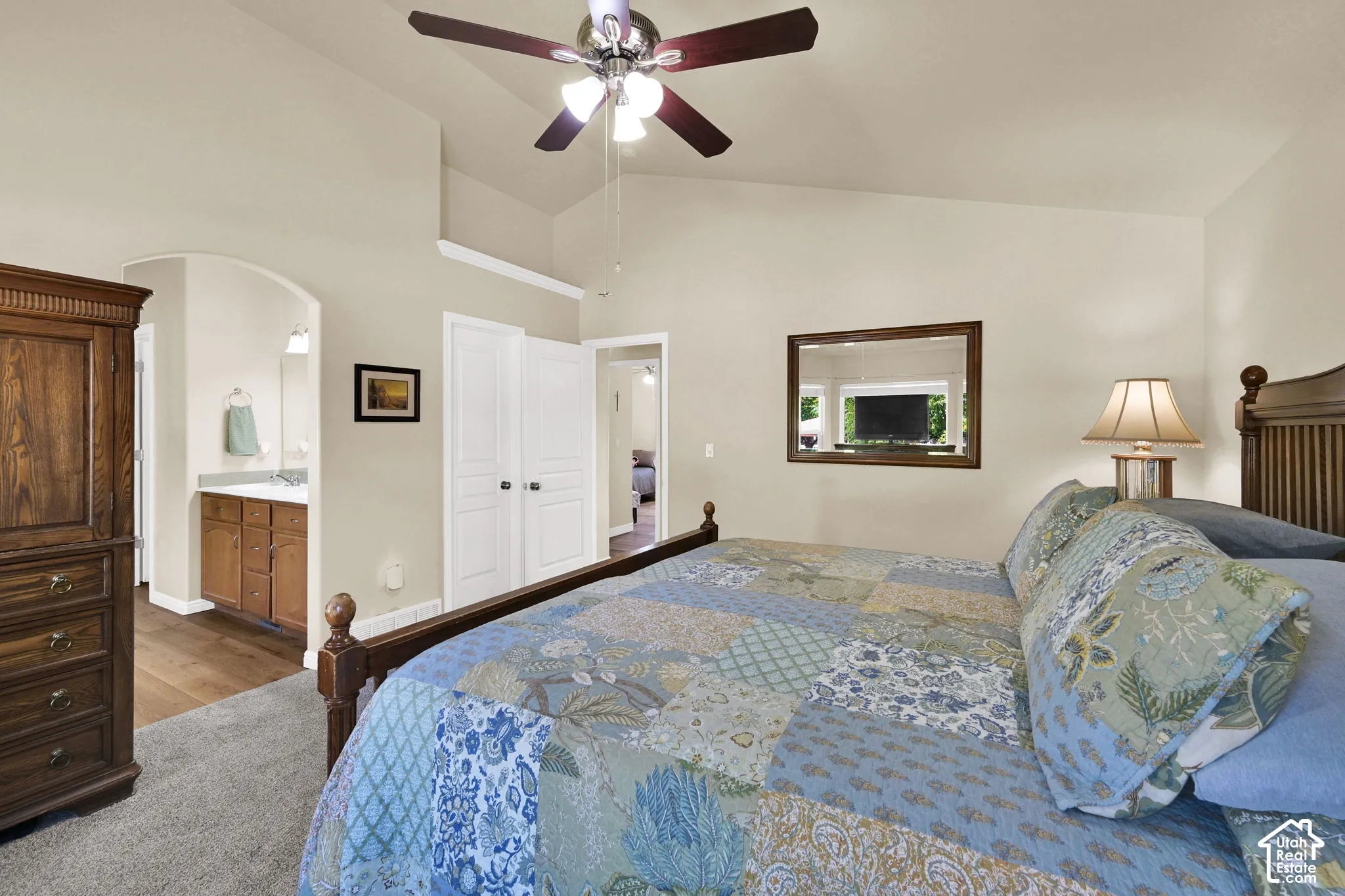 Vaulted ceiling with ceiling fan, arched doorway to a single vanity, wood-finish flooring, and white bifold doors