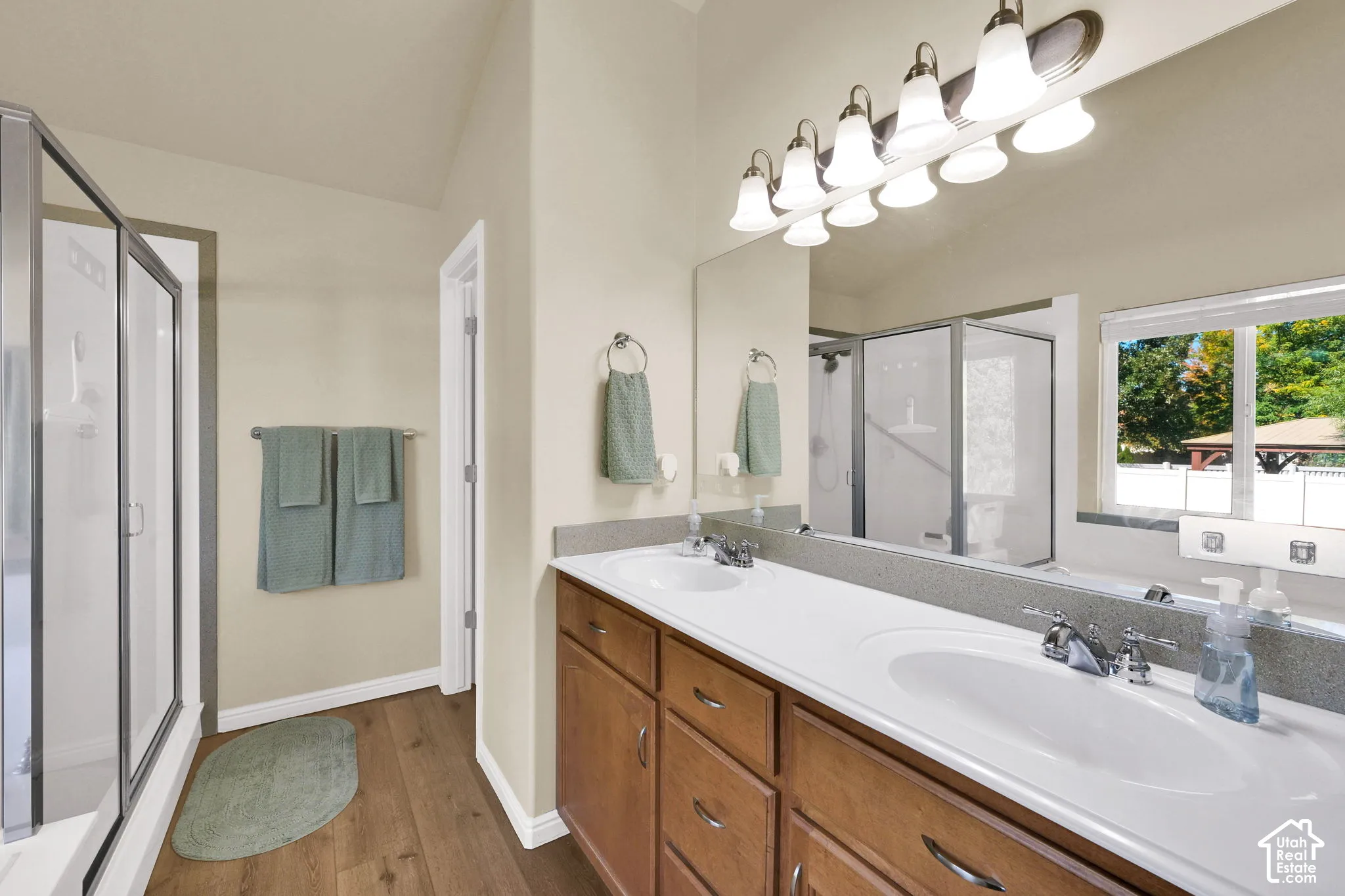 Dual vanity with integrated sinks, wood-finish cabinetry, a large frameless mirror, and a glass-enclosed shower