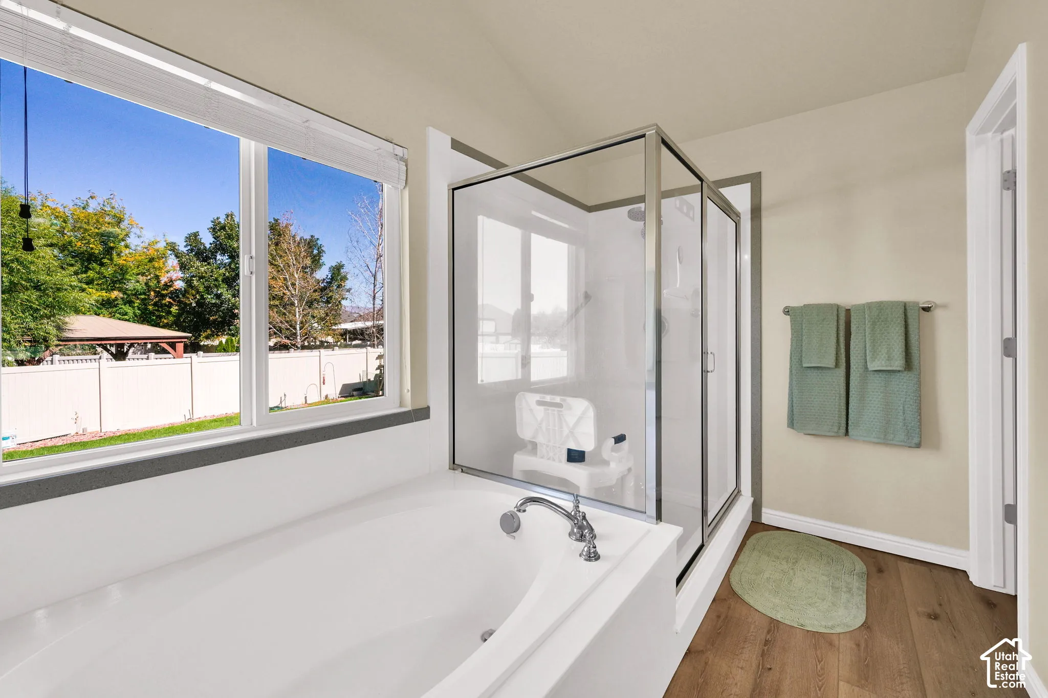 Soaking tub with a polished chrome faucet, adjacent to a glass-enclosed shower, and wood-finish flooring