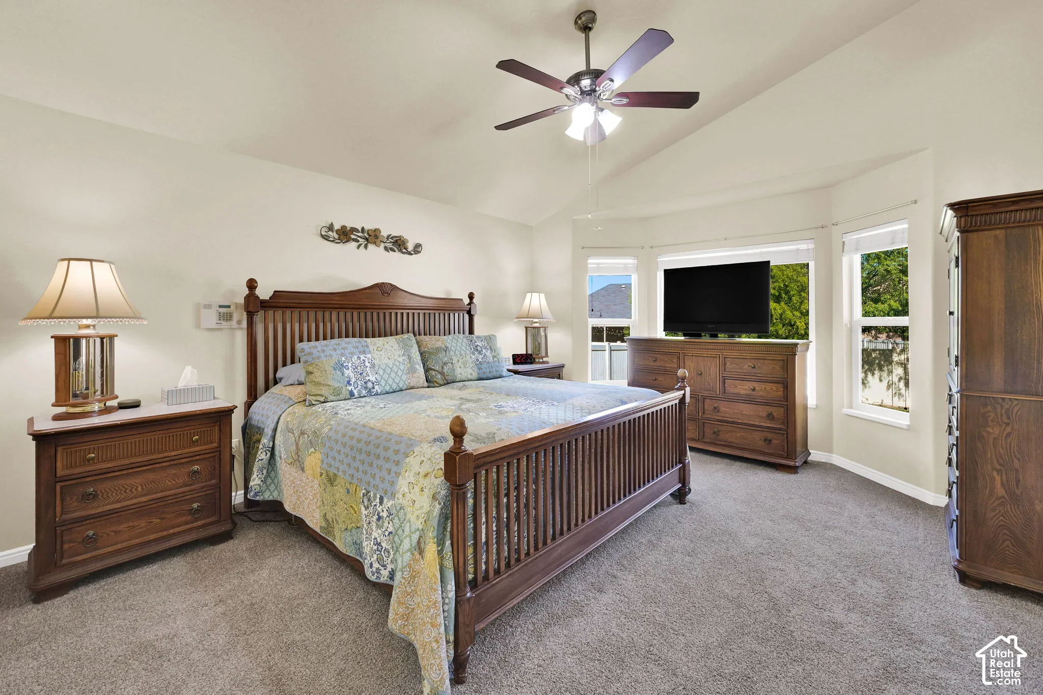 Vaulted ceiling, ceiling fan, carpeting, bay window, and light-colored walls