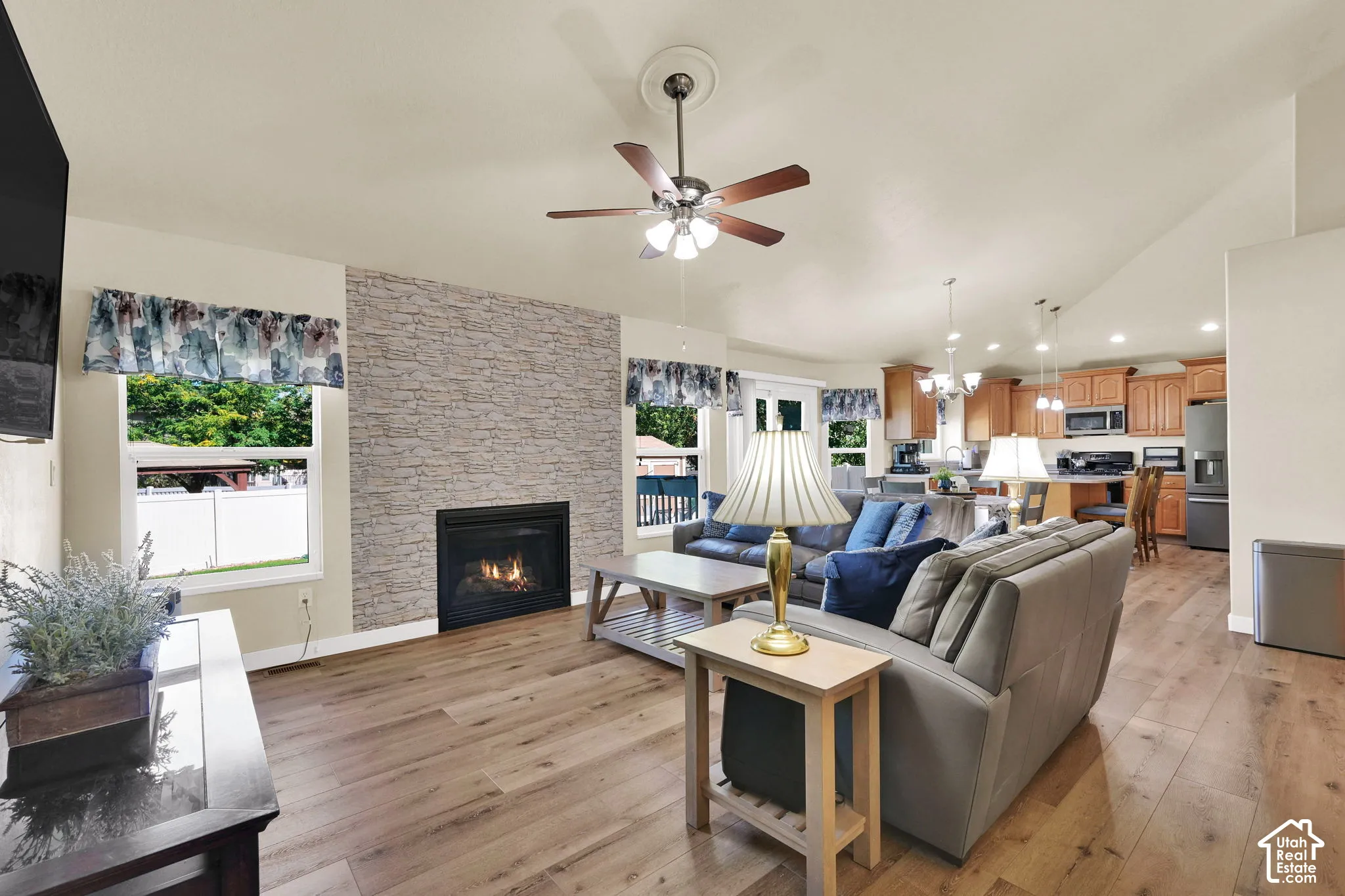 Living area with wood-finish flooring, a stacked stone fireplace, a ceiling fan, and recessed lighting