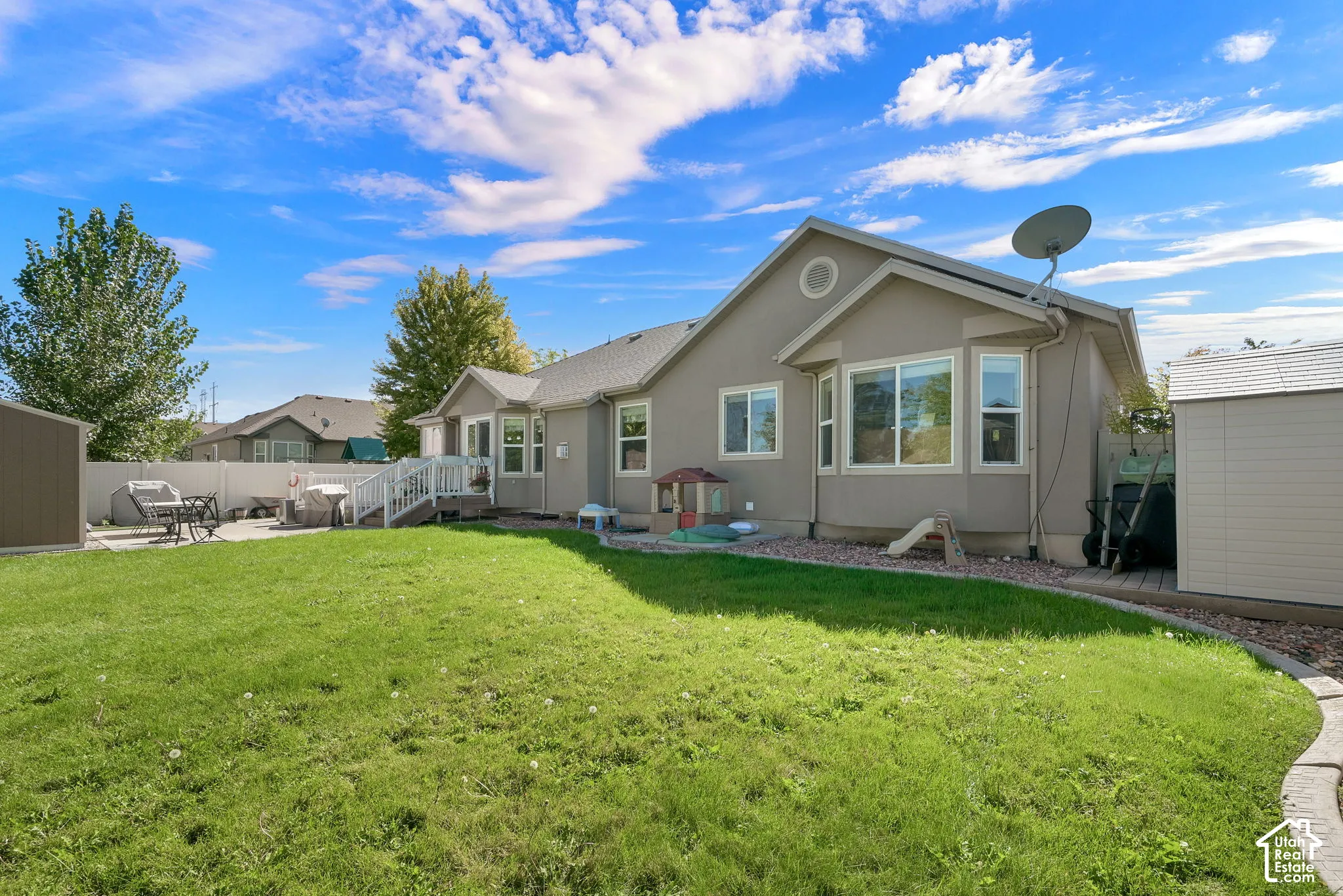 Expansive lawn area, concrete patio, white vinyl fencing, and two storage sheds