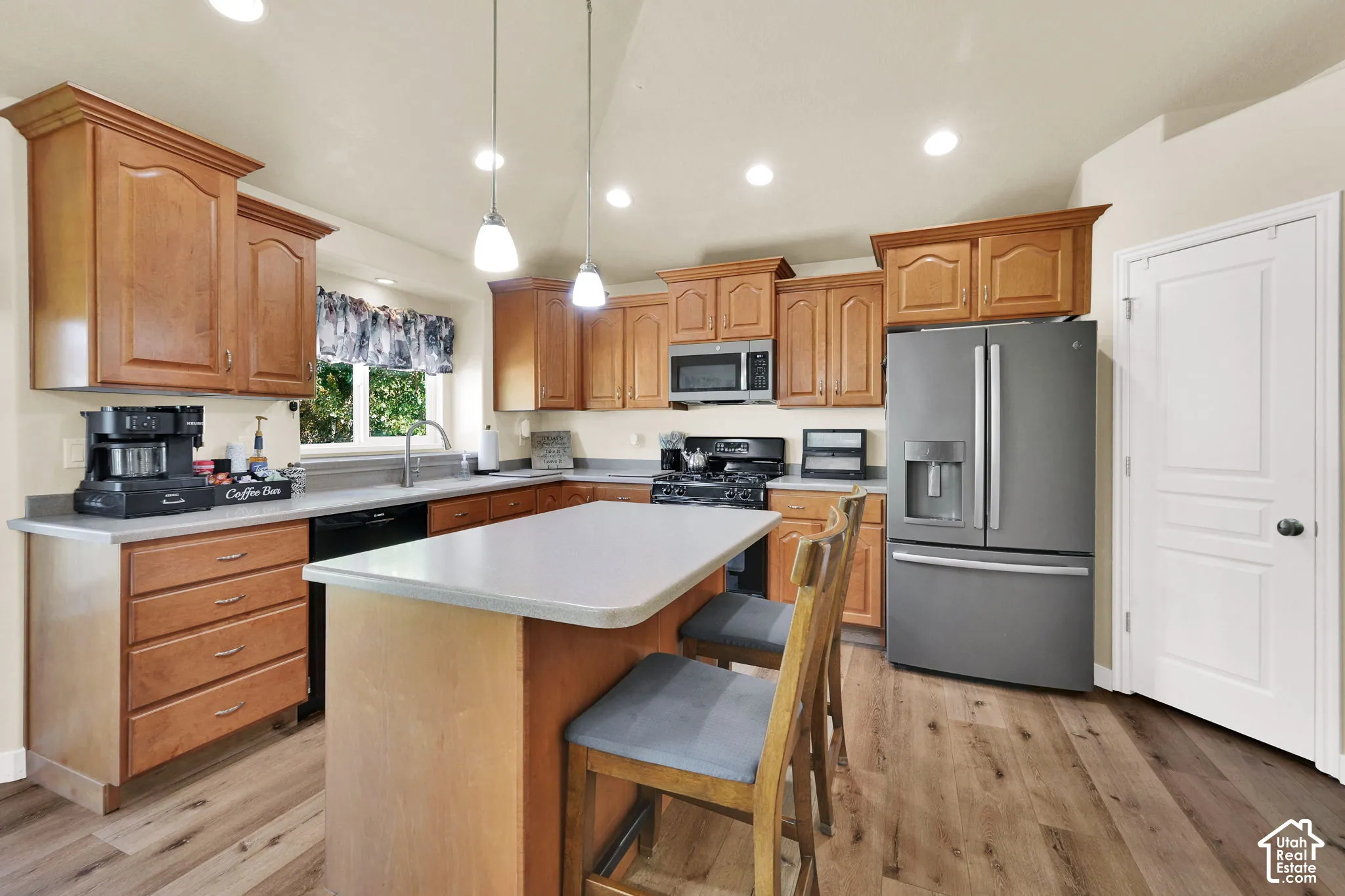 Kitchen with wood-finish flooring, light wood cabinetry, a center island with countertop seating, stainless steel appliances, and recessed lighting