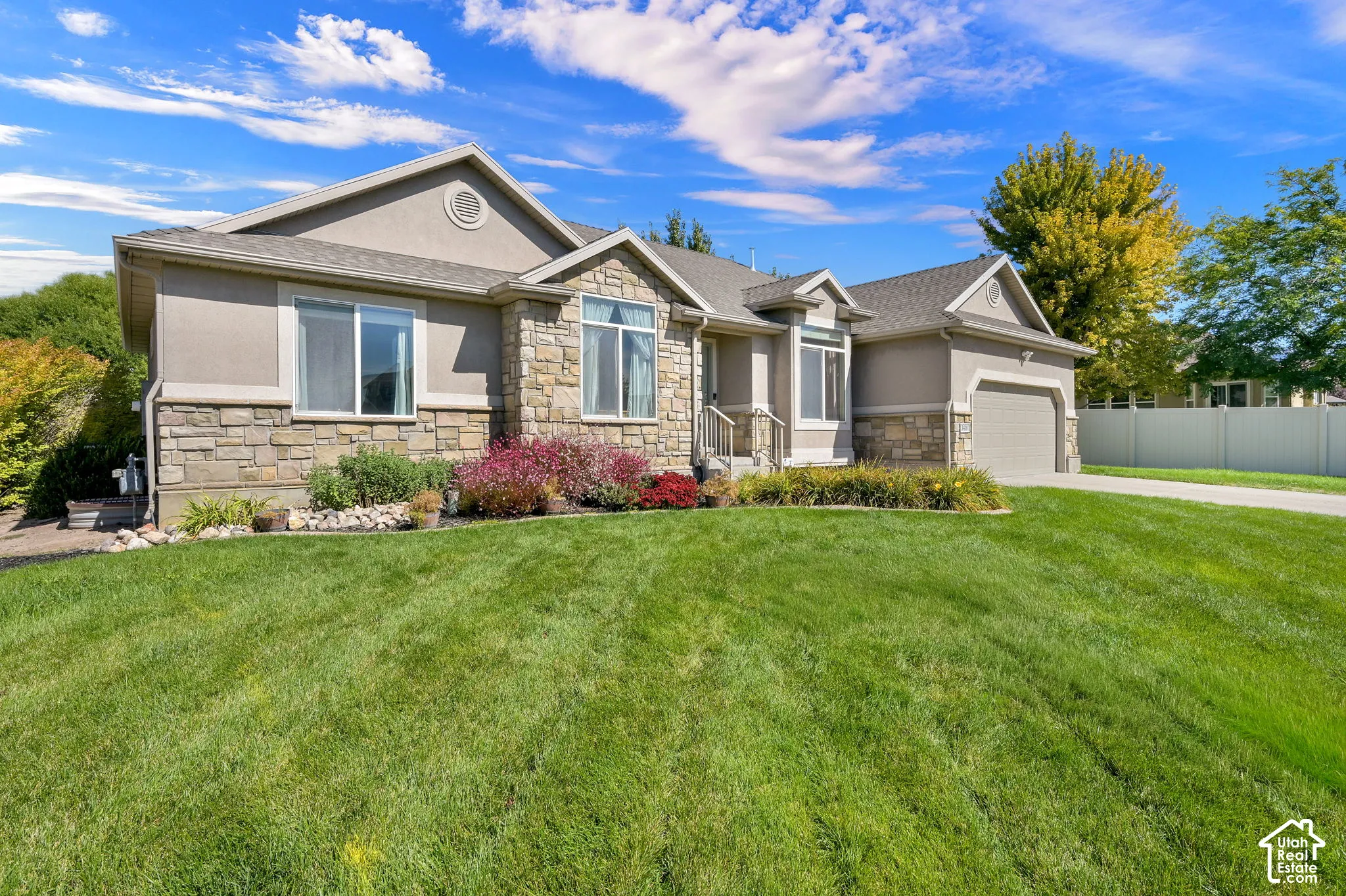 Stucco and stone exterior with an attached garage, paved driveway, and mature landscaping