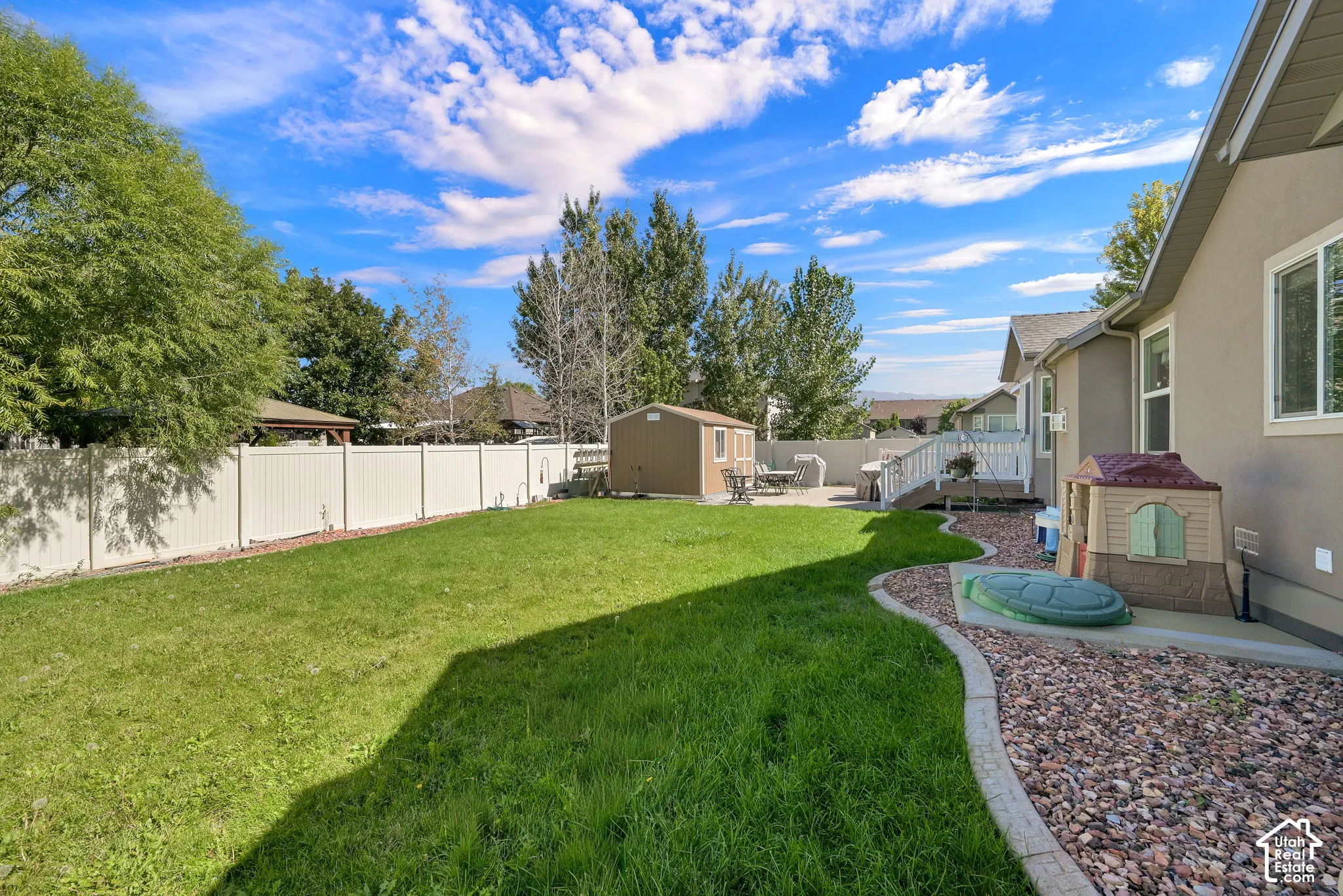 Expansive backyard with a manicured lawn, white privacy fencing, a storage shed, and a paved patio area