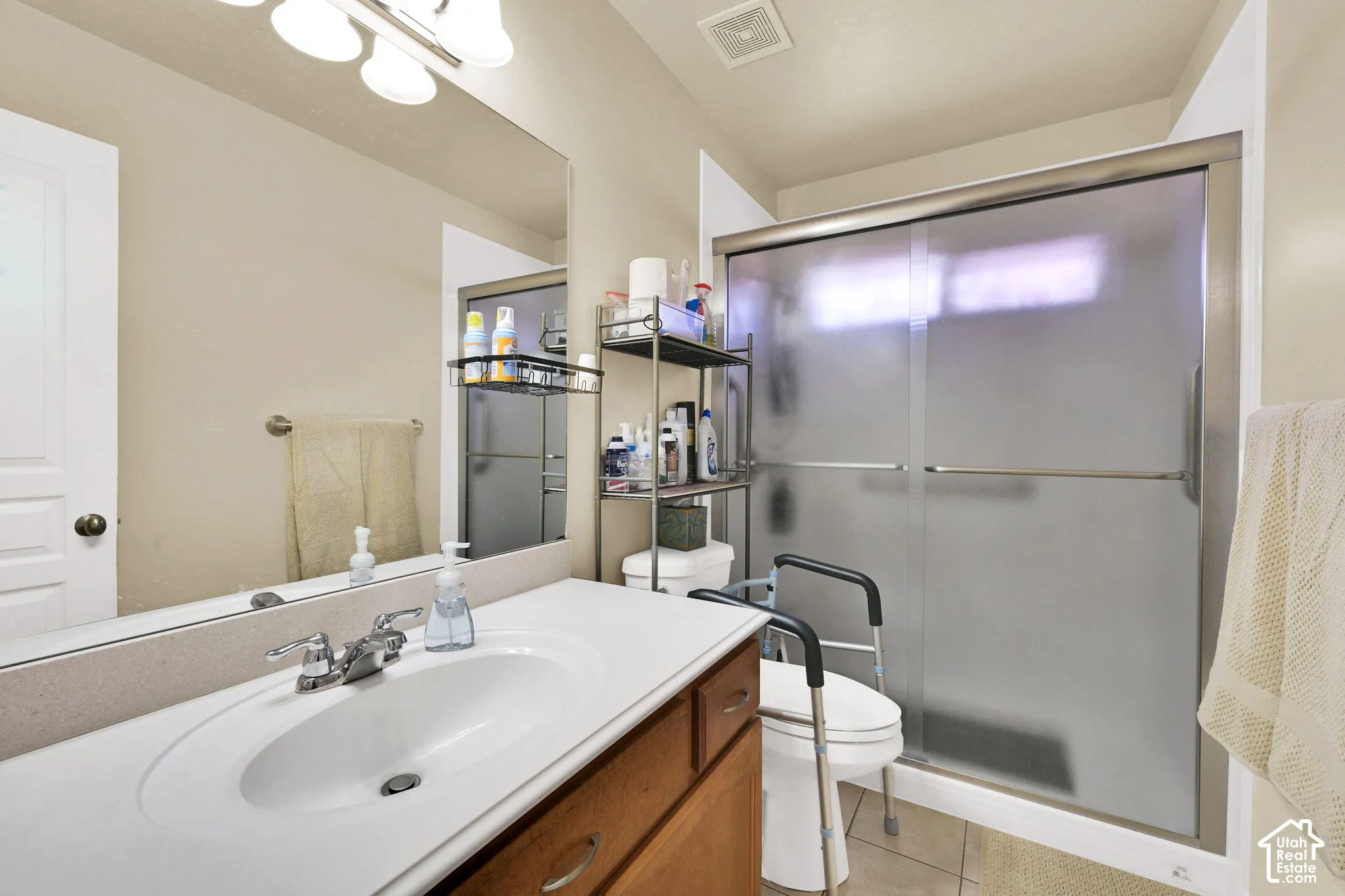 Bathroom featuring a single vanity with an integrated sink, polished chrome faucet, a large wall-mounted mirror, and a shower with frosted sliding glass doors