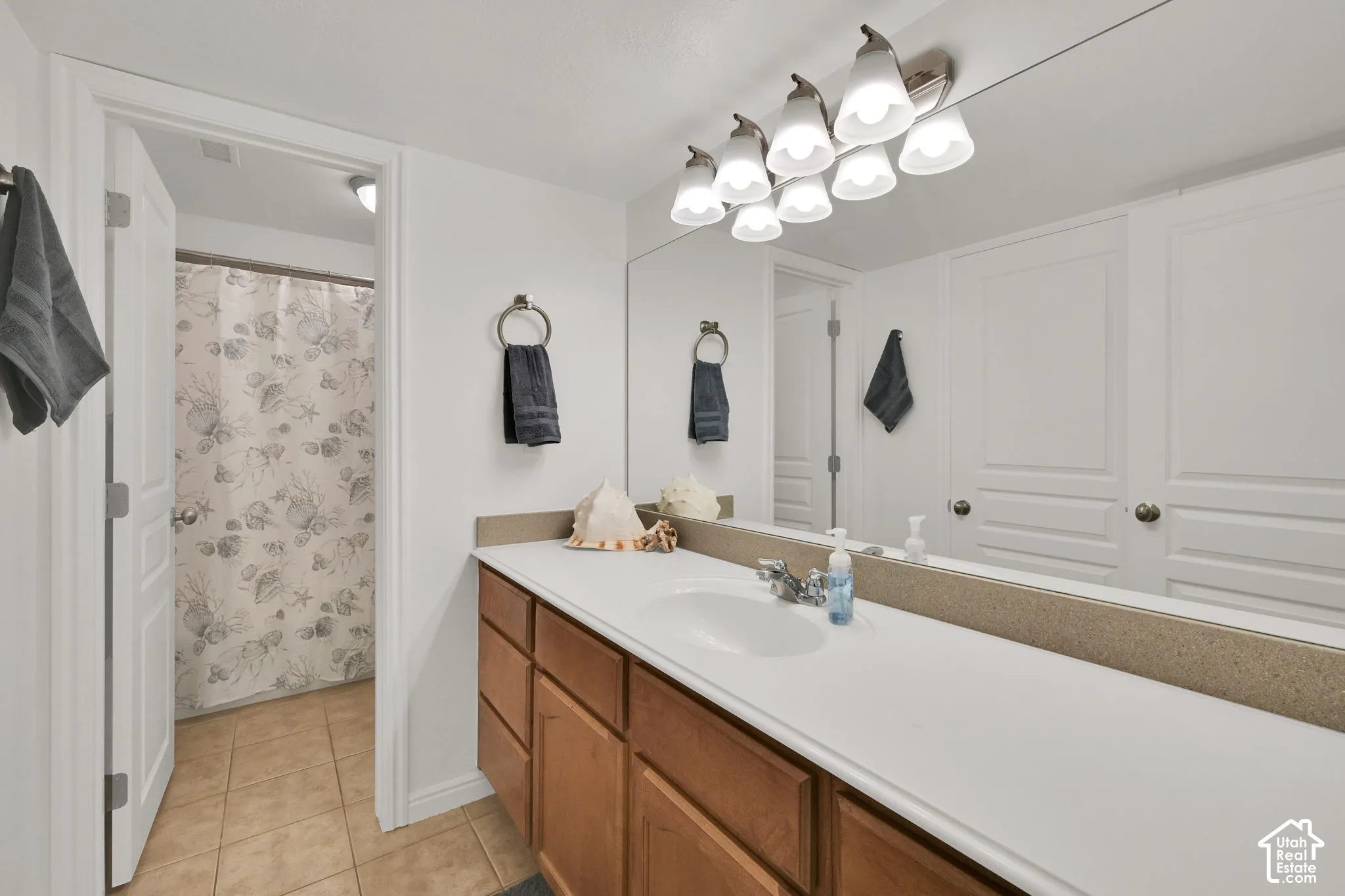 Extended vanity with integrated sink, full-width mirror, wood-finish cabinetry, and tiled flooring