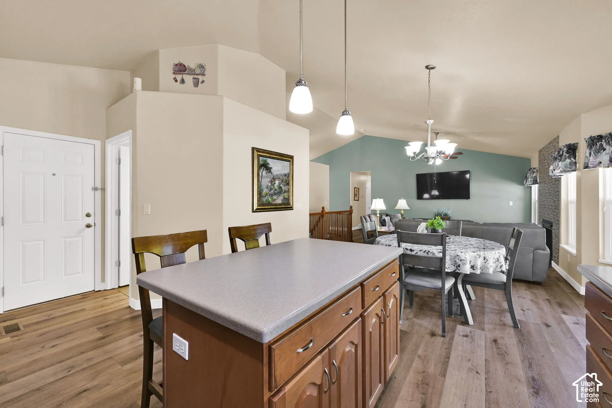 Kitchen island with integrated cabinetry and pendant lighting, wood-finish flooring, vaulted ceilings, and an open-concept living area