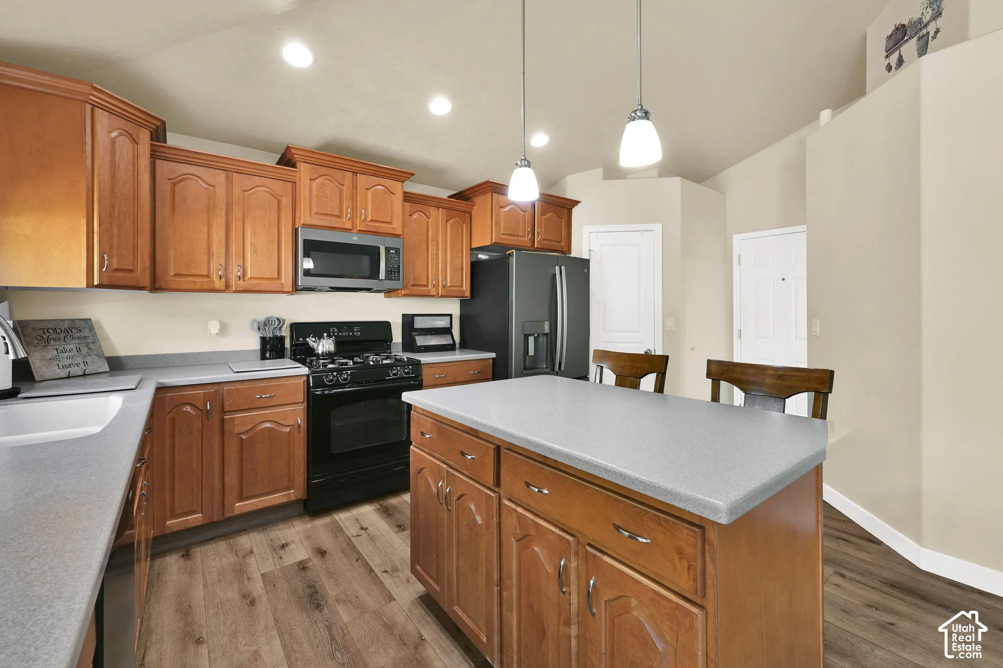 Kitchen featuring wood-finish cabinetry, a central island with countertop seating, stainless steel microwave, black gas range, and wood-finish flooring