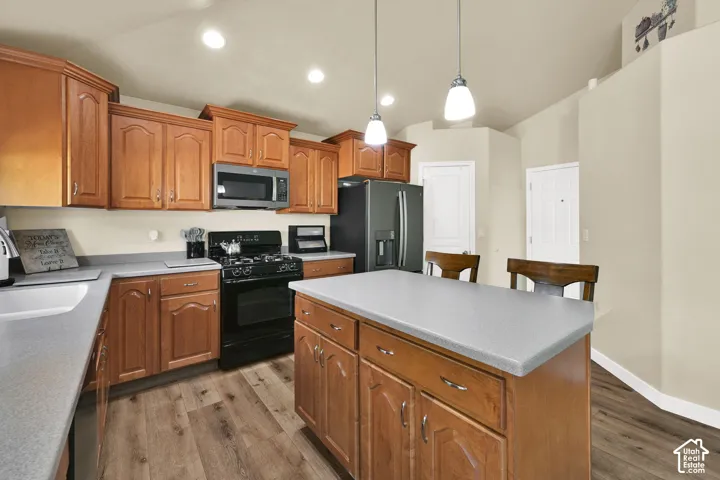 Kitchen featuring wood-finish cabinetry, a central island with countertop seating, stainless steel microwave, black gas range, and wood-finish flooring