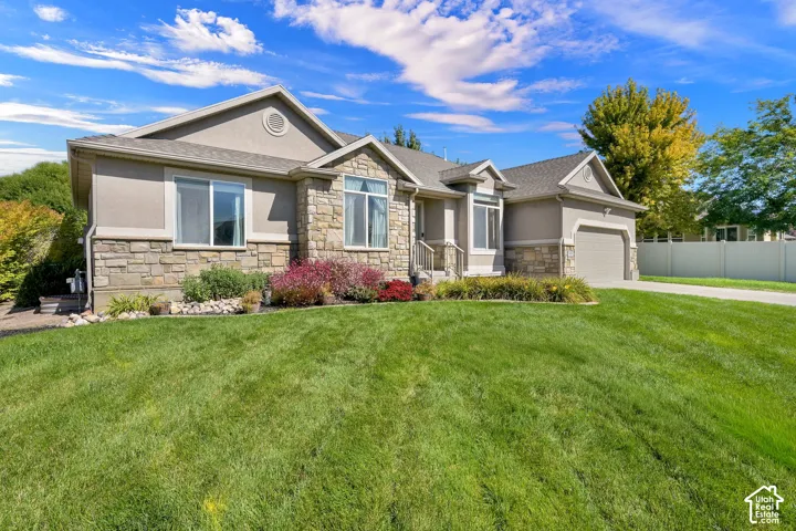 Stucco and stone exterior with an attached garage, paved driveway, and mature landscaping