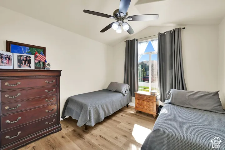 Vaulted ceiling featuring a ceiling fan with integrated lighting, wood-finish flooring, and a large window