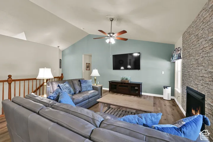 Vaulted ceiling, stone-clad fireplace, wood-finish flooring, ceiling fan, and wooden railing