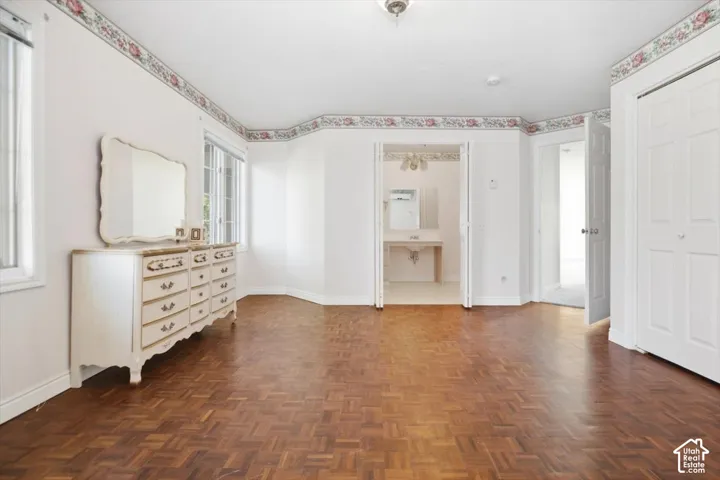 Herringbone wood-finish flooring, white walls with floral border, white trim windows, white paneled bifold closet doors, and an attached vanity with a single sink