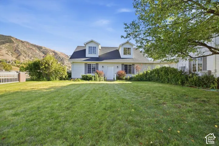 White siding exterior with a dark shingle roof, twin dormer windows, and a prominent front lawn