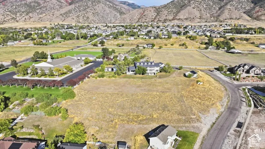 Expansive undeveloped lot with sloping terrain and mountainous backdrop, surrounded by residential properties and paved roads