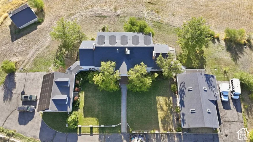 Expansive lot featuring a primary residence with solar panels, a detached structure with solar panels, an additional detached structure, a manicured lawn, and mature trees