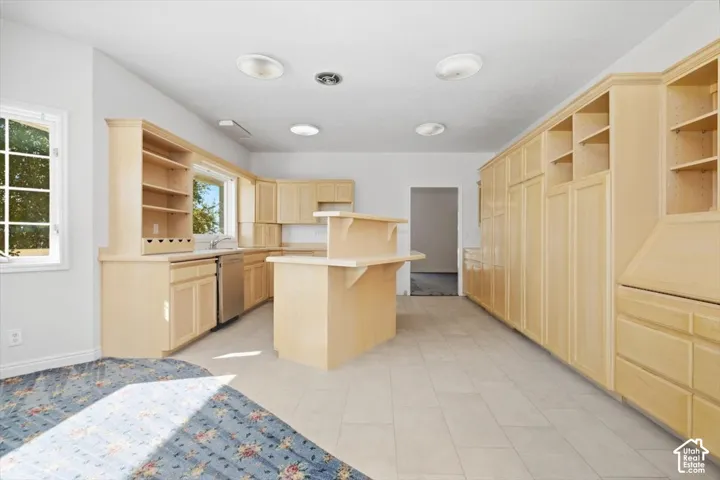 Expansive kitchen area featuring extensive light wood cabinetry, a center island with breakfast bar, tiled flooring, and multiple windows