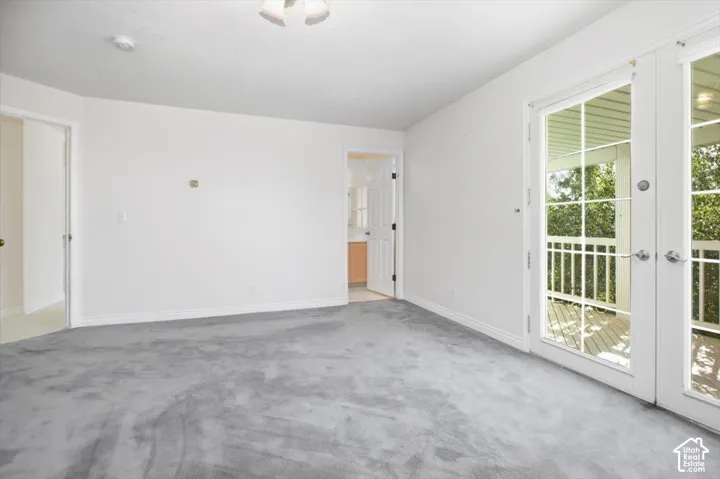 Carpeted room with white walls, ceiling-mounted light fixture, and double glass-paneled doors opening to an exterior balcony