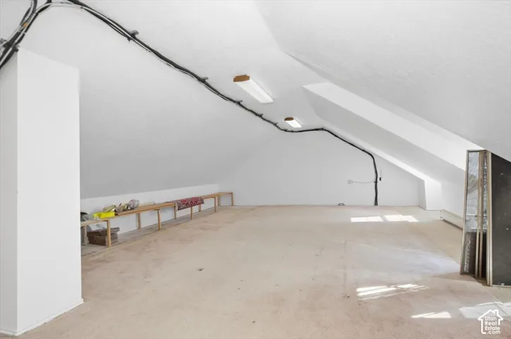 Spacious attic area with sloped ceilings and light-toned carpeting