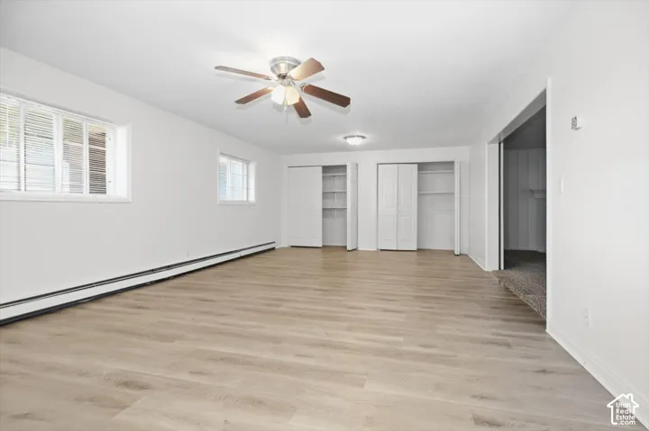 Wood-finish flooring, two windows with horizontal blinds, ceiling fan with integrated lighting, recessed lighting, and two built-in closet systems