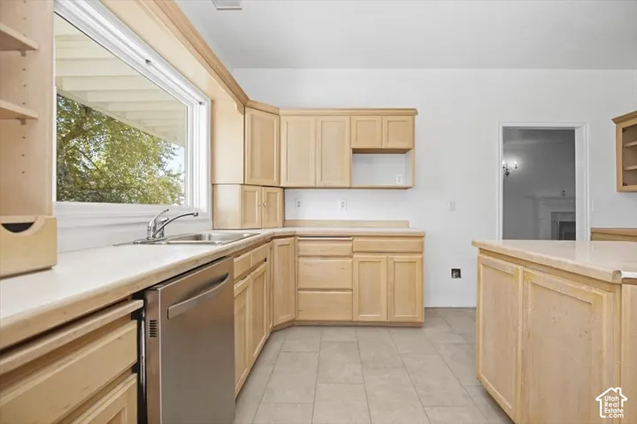 Kitchen featuring light wood cabinetry, light countertops, stainless steel dishwasher, and tiled flooring
