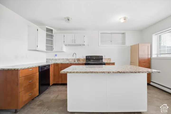 Kitchen featuring a central island, granite countertops, wood-finish cabinetry, white upper cabinets, and a black range