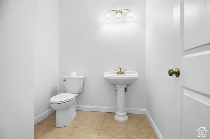White pedestal sink with brass-finish faucet, white toilet, and tile flooring