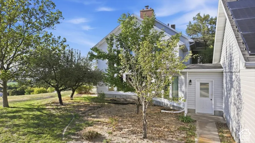 White siding exterior with a brick chimney and mature trees