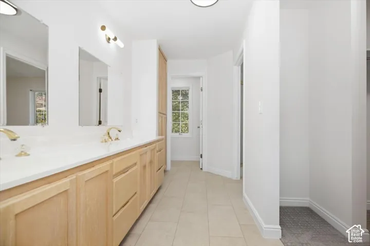 Double vanity with light wood cabinetry, white countertop, dual gold-tone faucets, and two mirrors