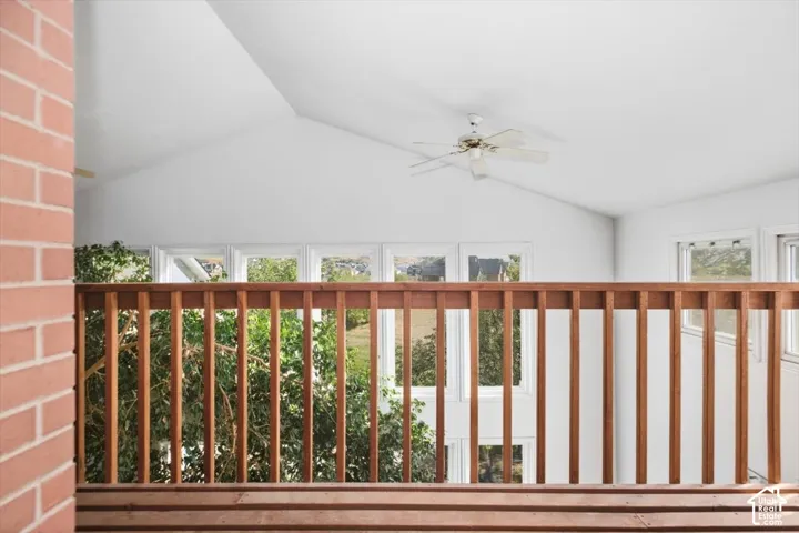 Vaulted ceilings with a ceiling fan, wood railing, and multiple windows providing natural light