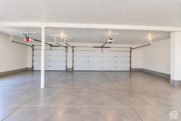 Concrete flooring, dual garage doors, white walls, overhead lighting, garage door openers