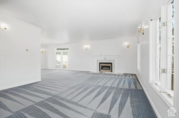 Spacious interior with an ornate fireplace, multiple sconce fixtures, a chandelier, and double French doors with transom windows