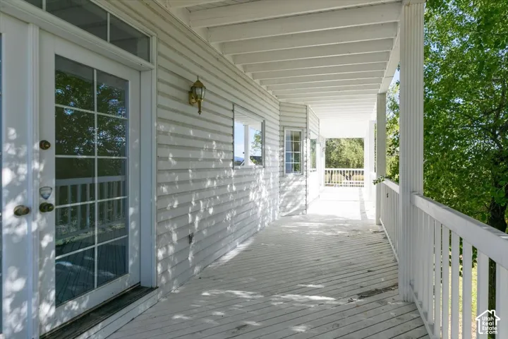 Expansive covered porch with white siding, decorative outdoor lighting, multiple windows, and a glass-paneled door
