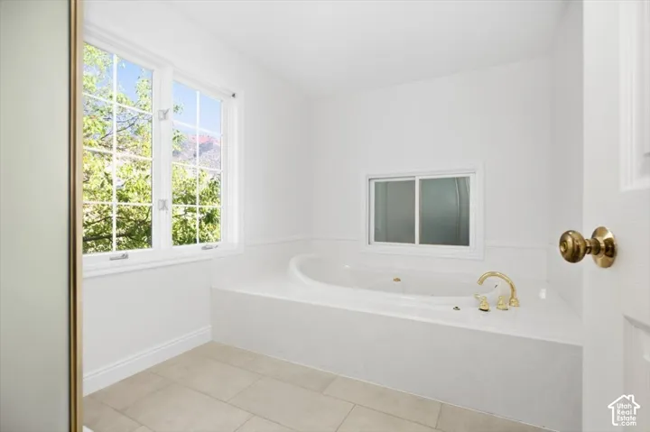 Soaking tub with brass fixtures, white tile surround, and a large grid-pattern window