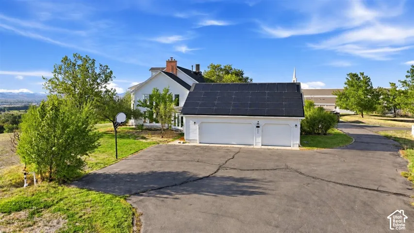 Two-car garage with installed solar panels, a paved driveway, and established landscaping