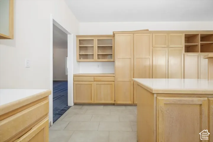 Kitchen featuring light wood-finish cabinetry, glass-front upper cabinets, light-toned countertops, and tile flooring
