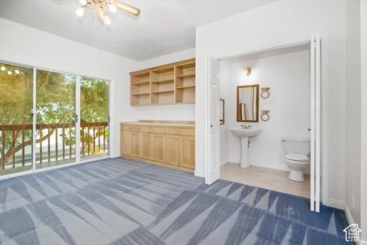 Sliding glass doors opening to a wood-railed balcony, built-in wooden cabinetry with open shelving, and a separate room featuring a pedestal sink and toilet