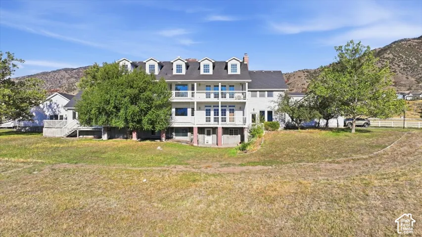 Multi-level residence featuring a dormered roofline, multiple balconies, a lower-level patio, and an expansive yard