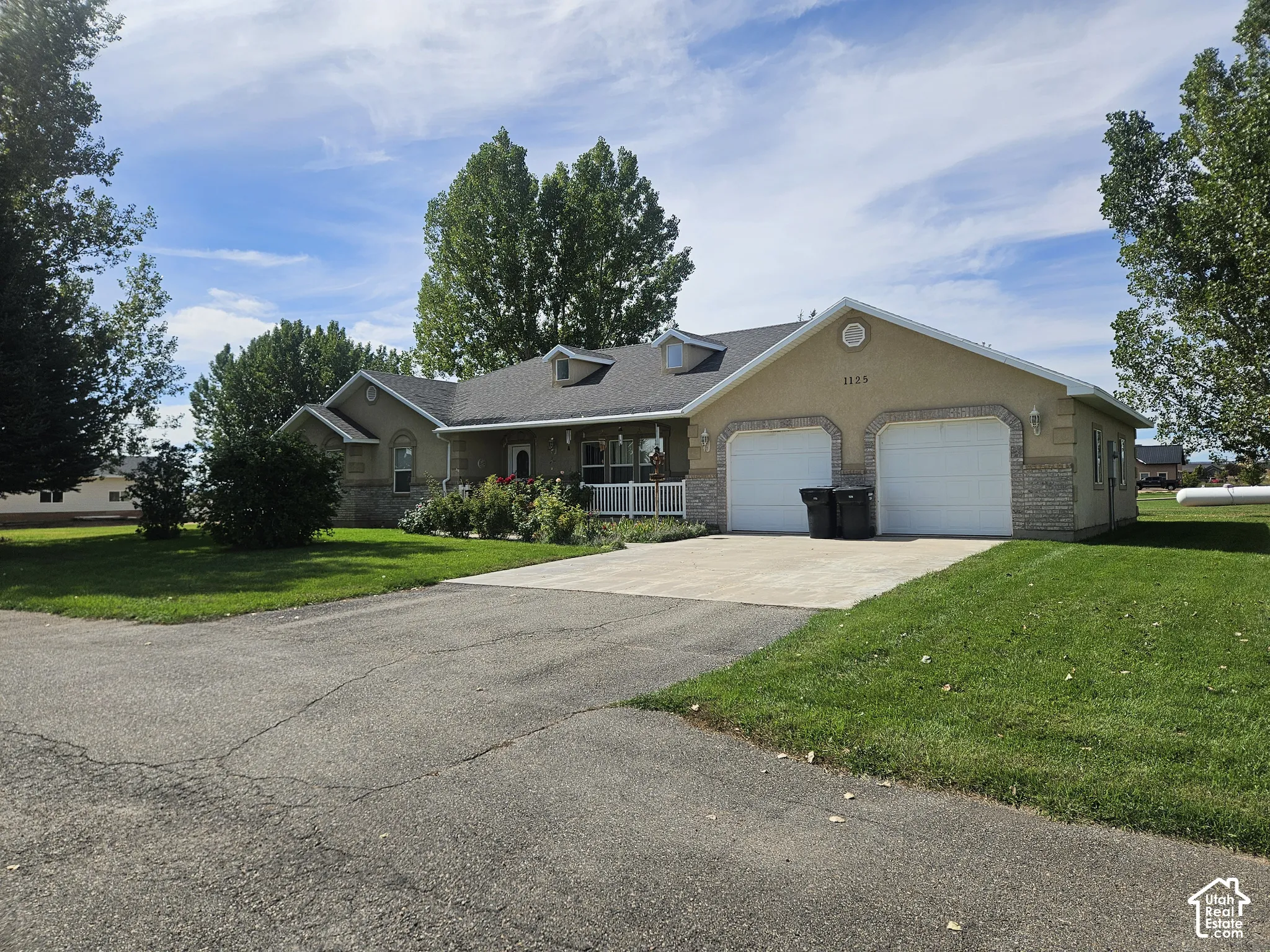 Two-car garage with a concrete driveway, a front porch with white railing, and a gabled roofline