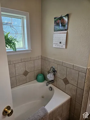 Built-in soaking tub with chrome fixtures, surrounded by tiled walls featuring decorative inlays, and a window with a patterned glass insert