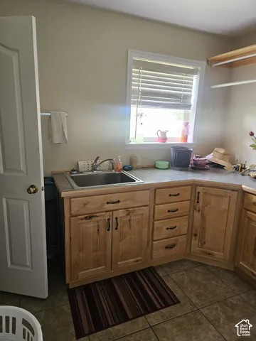 Light-toned wood cabinetry, stainless steel sink, tiled flooring, and a window with blinds