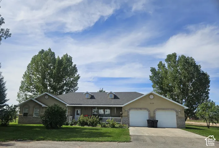 Ranch-style residence featuring a dormer roof, stucco and stone-veneer facade, covered porch, and an attached two-car garage