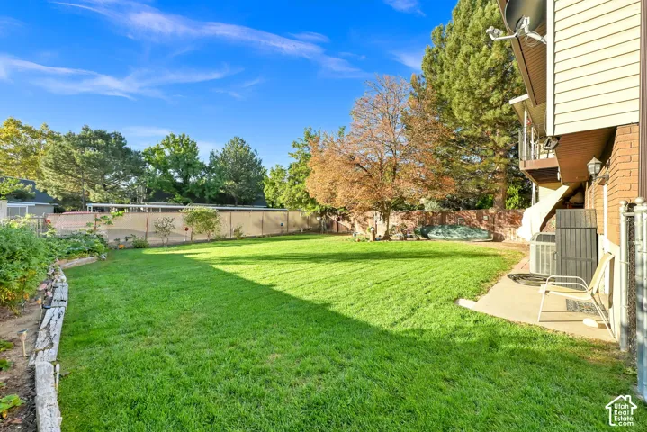 Expansive backyard featuring a lush lawn, mature trees, and a concrete patio