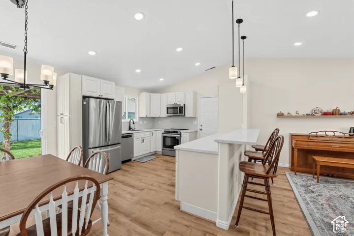Kitchen featuring light cabinetry, stainless steel appliances, a white island with bar seating, and wood-finish flooring