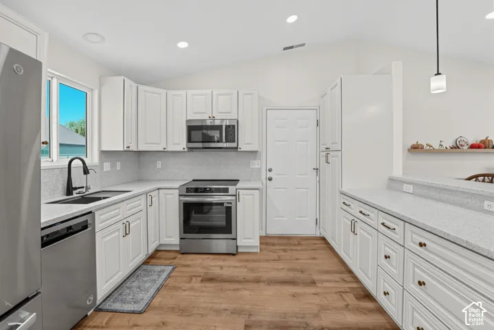 Vaulted ceilings, white shaker cabinetry, stainless steel appliances, wood-finish flooring, and light-toned countertops
