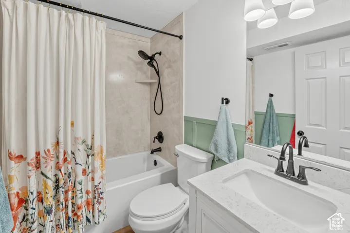 Bathroom featuring a white bathtub, light-colored shower surround, white toilet, vanity with a white countertop, and dark-toned fixtures