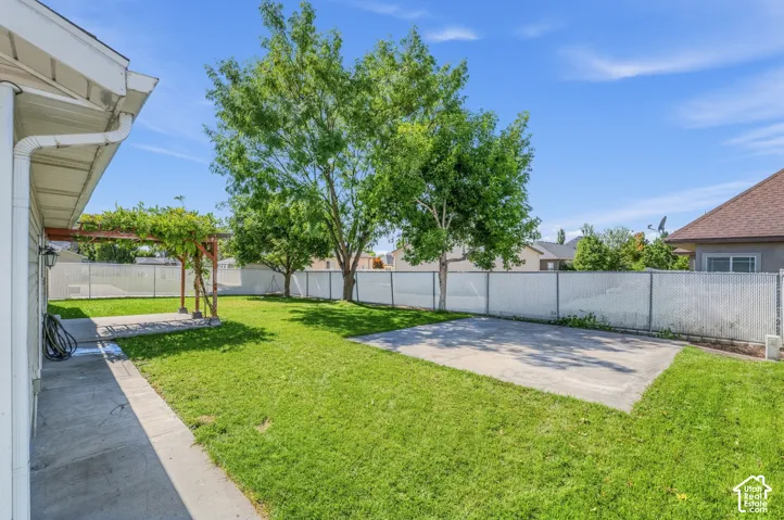 Expansive backyard featuring a lush lawn, mature trees, a concrete patio, and a covered pergola