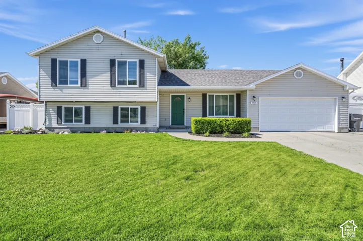 Siding exterior with dark shutters, attached two-car garage, and a lush lawn
